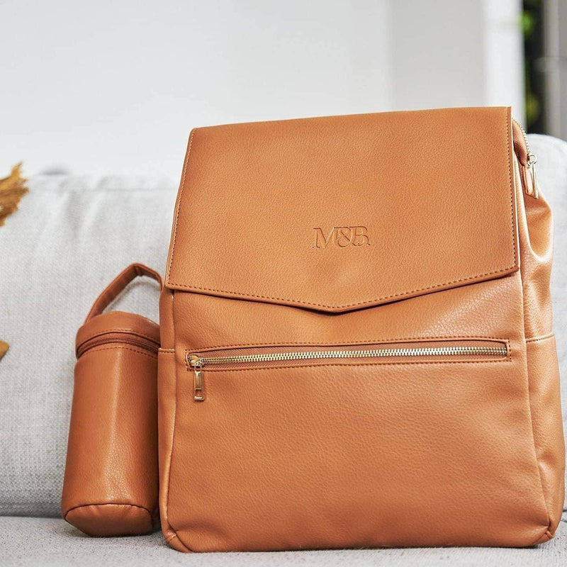 A Scarlett - Caramel leather backpack on a couch by Mother and Baby.