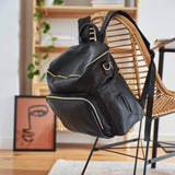 An Ava - Black backpack sits on a chair in a living room, produced by Mother and Baby.