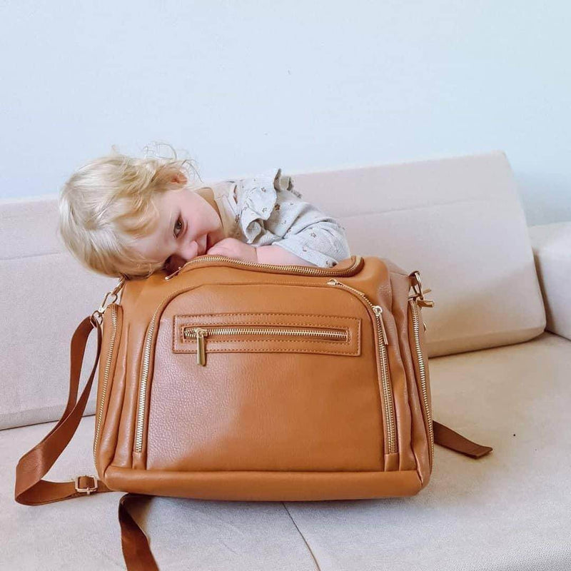 A little girl laying on top of a Chloe - Caramel bag from Mother and Baby.