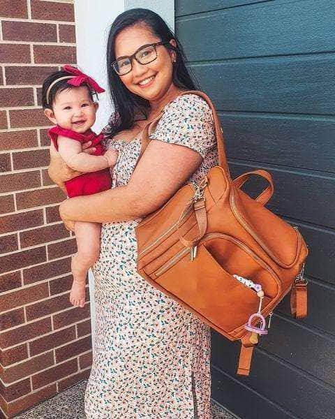 A woman with a baby holding a Chloe - Caramel diaper bag, made by Mother and Baby.