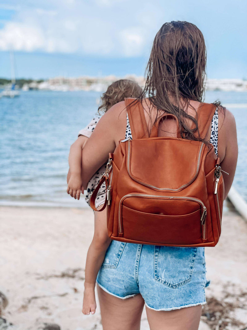 A woman wearing a Chloe - Caramel diaper bag by Mother and Baby on the beach.