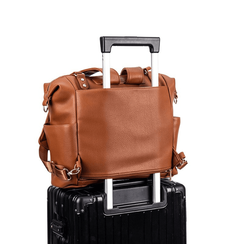 An Ivy - Caramel leather bag on top of a black suitcase from Mother and Baby.