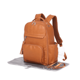 A tan leather Olivia - Caramel backpack with a Mother and Baby diaper bag on top.