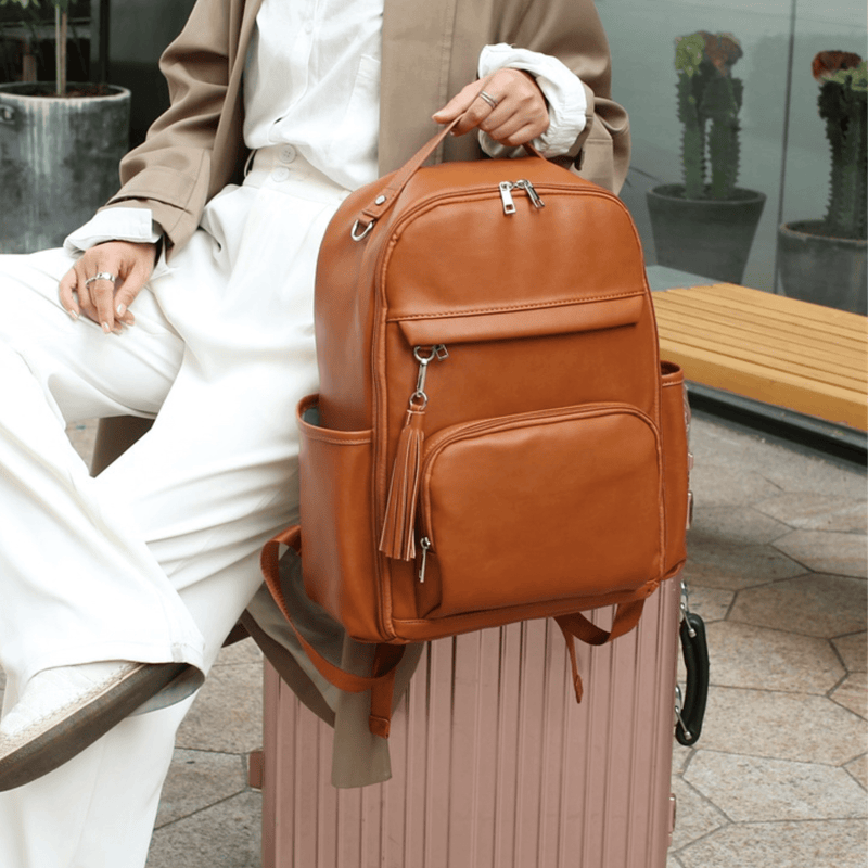 A woman with a Caramel Olivia backpack sitting on a suitcase.