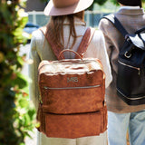 A woman wearing a Willow - Tan hat and carrying a Mother and Baby backpack.