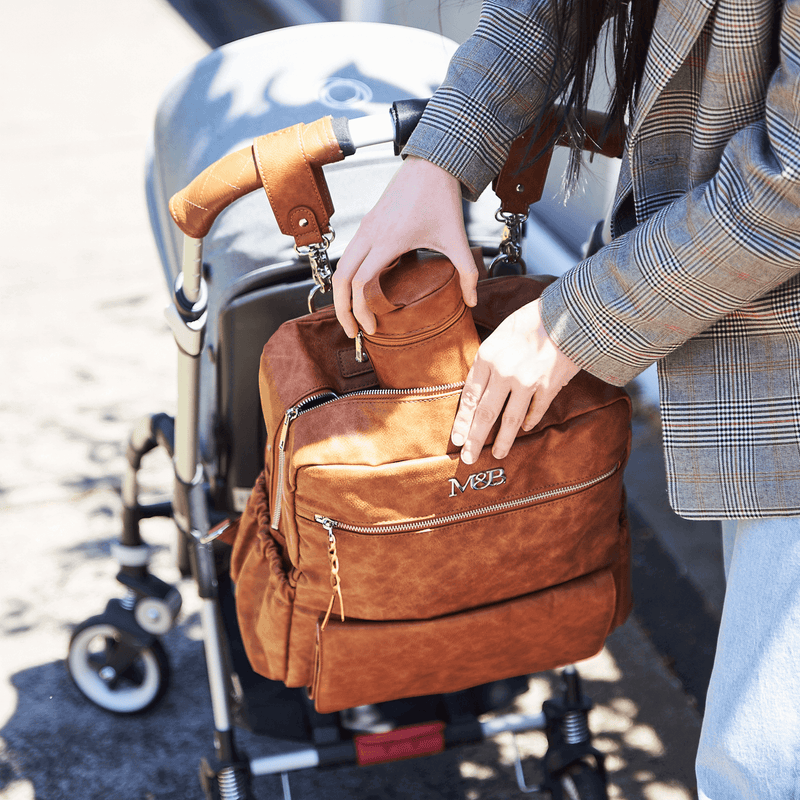A woman pushing a stroller with a Mother and Baby - Willow - Tan bag.
