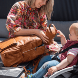 A woman with a baby in a wheel chair holding a Mother and Baby - Willow - Tan bag.