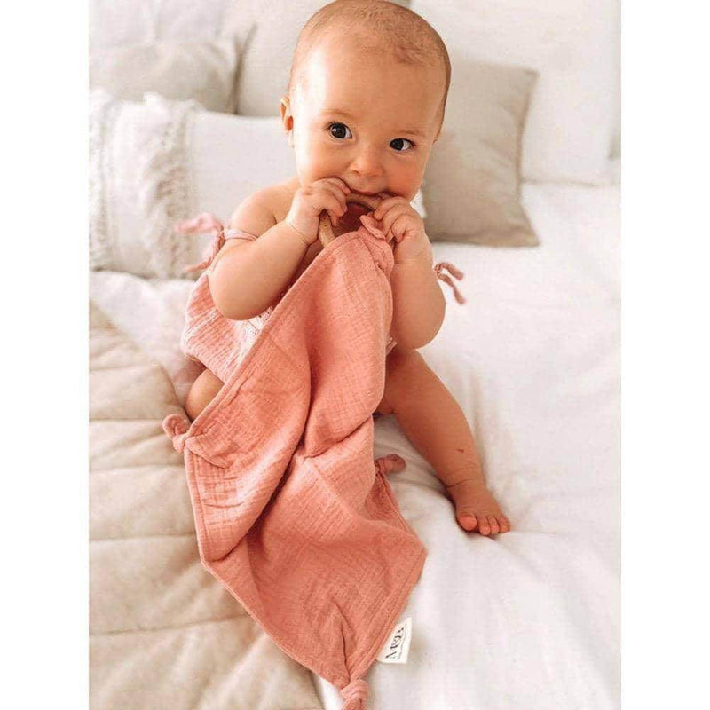 A baby is sitting on a bed with a Mother and Baby Comforter Swaddle.