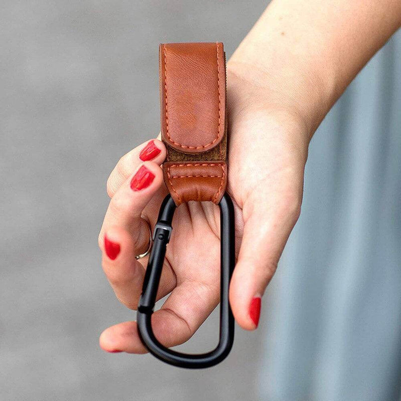 A woman holding a Mother and Baby brown leather Luxe Stroller Strap carabiner.