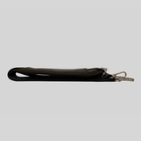 A Mother and Baby Padded Adjustable Shoulder Strap - Black hanging on a gray background.